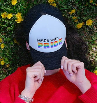 Girl covers her face with Made with Pride hat by Makeship