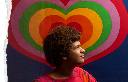 A boy with a rainbow-coloured heart behind him